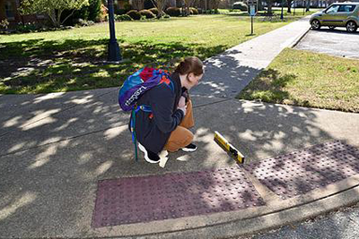 A person with a backpack kneeling down on a sidewalk ramp to monitor a level