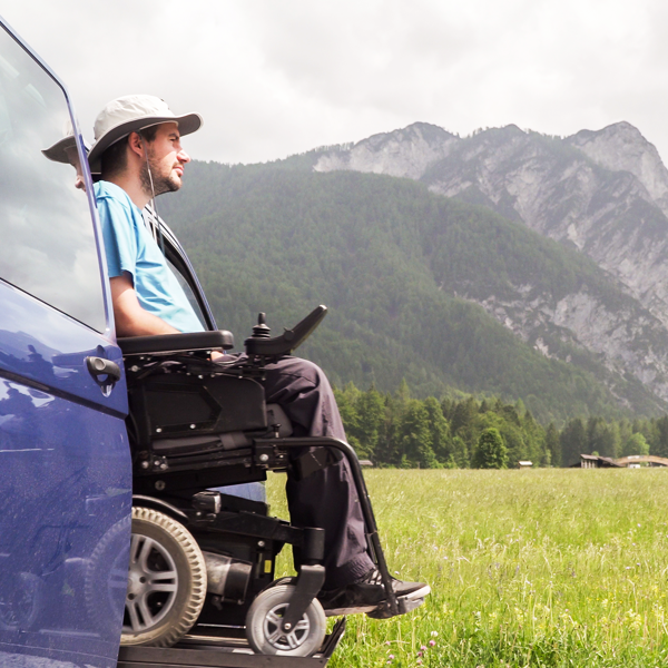 A man in a wheelchair exiting a vehicle on a ramp, with mountains in the background